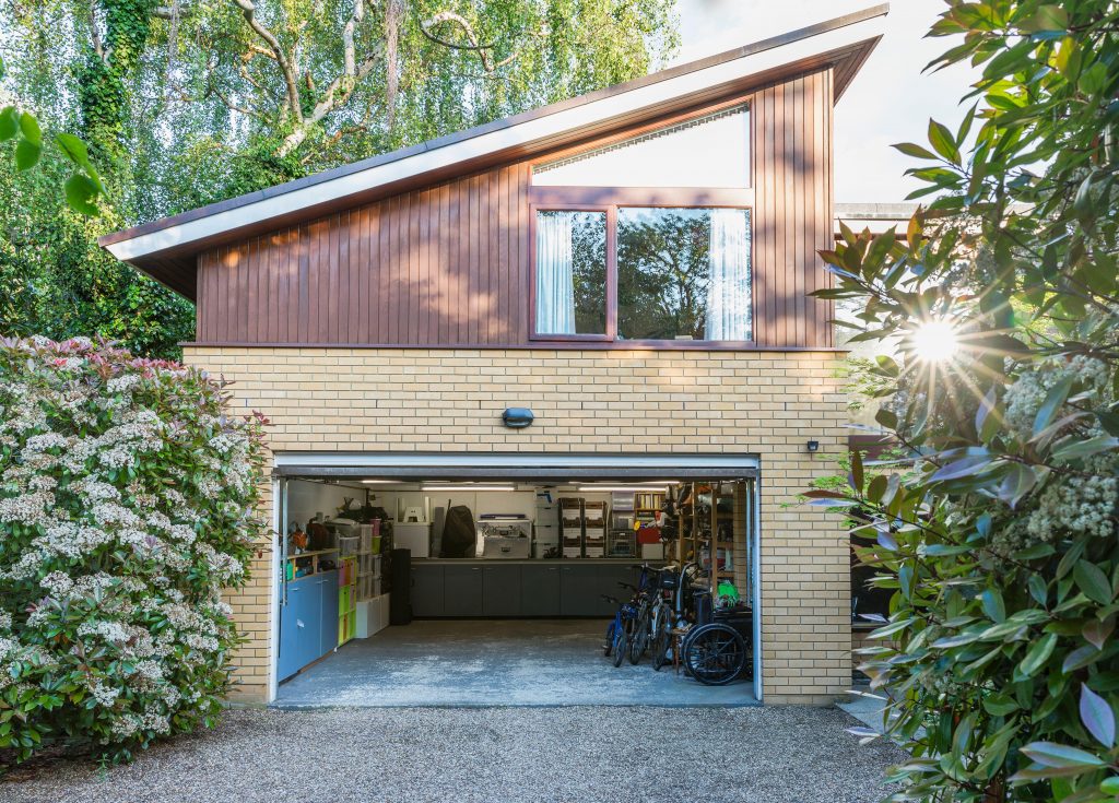 A shot of an open garage that is neatly organized. The driveway leading up to the garage is flanked by rich green plants and trees