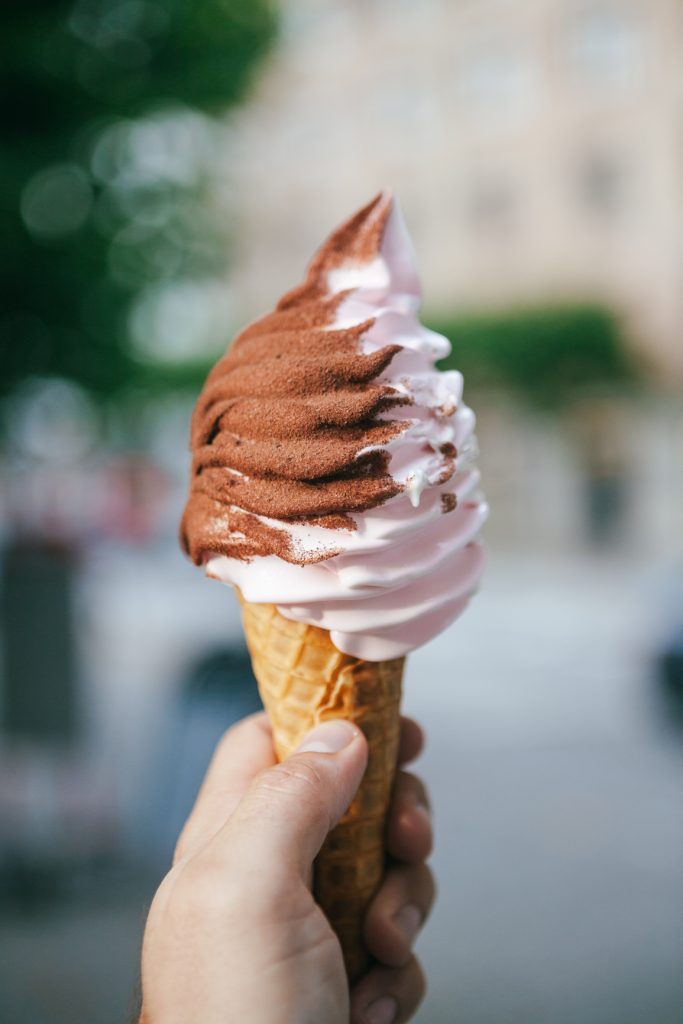 a hand holds a chocolate and vanilla soft serve ice cream