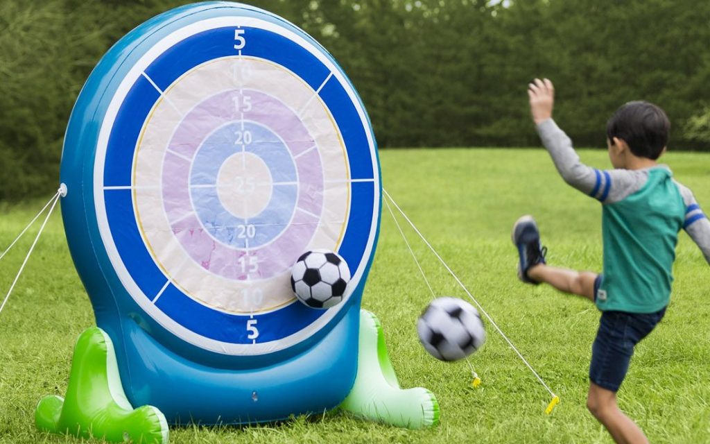 An action shot of a child kicking a socker ball at a blow up target in a backyard during summer
