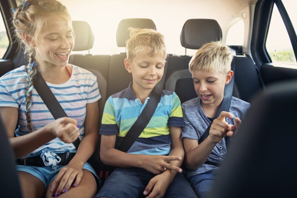 Three young children play road trip games in the backseat of a card