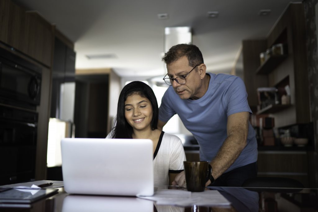 A father helps his daughter on a computer happily, explaing her insurance policy