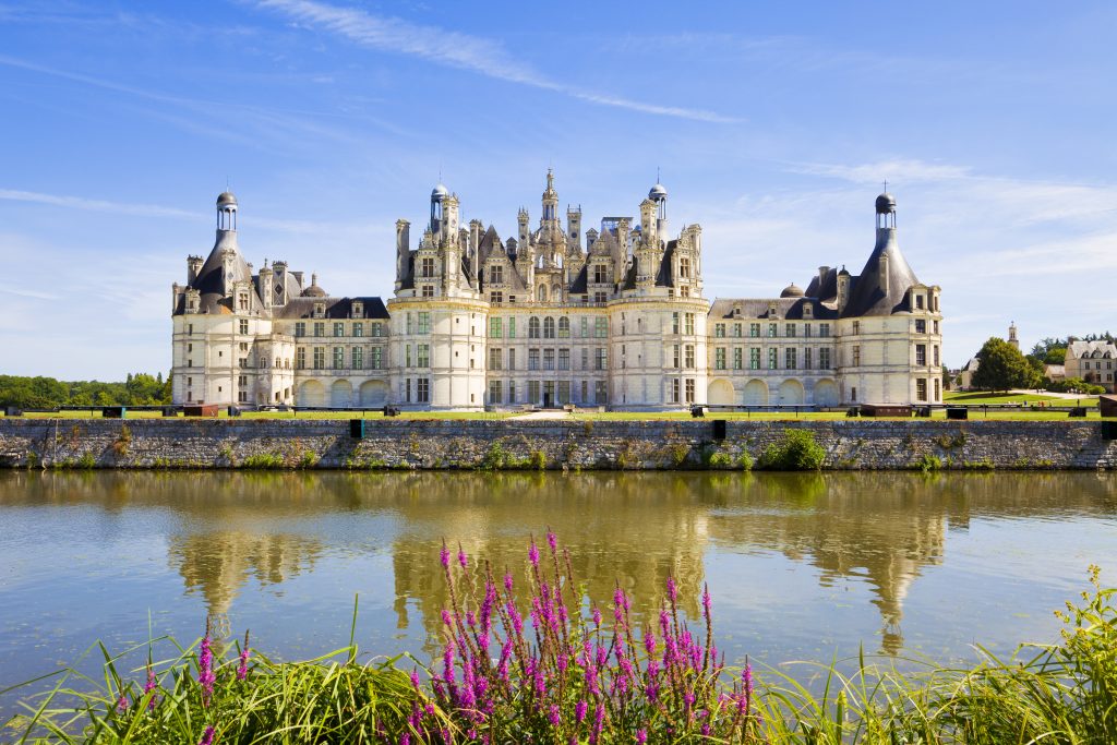 "Chambord, France - July 31, 2009: Great panoramic of Chambord Chateau reflected in the canal in a summer day with blue sky. There are some unrecognizable people in the balconies"