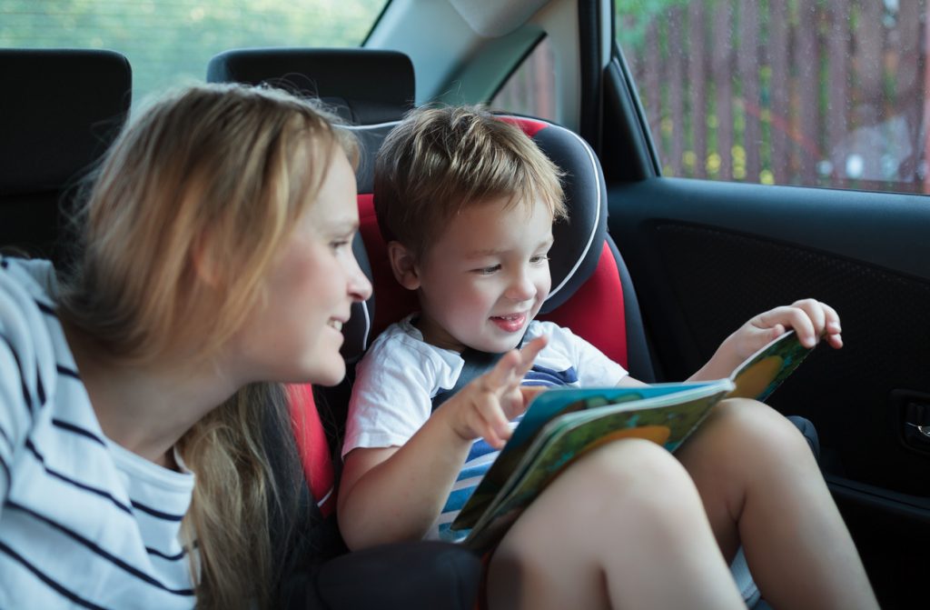 A young child and his mom reading a book in a car and playing road trip games