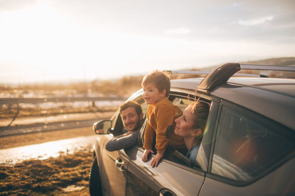 A young family embarks on a road trip. The family admires the view out their car windows as the golden sun sets