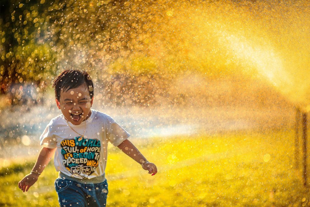 A young boy runs happily through a sprinkler in the summer sun