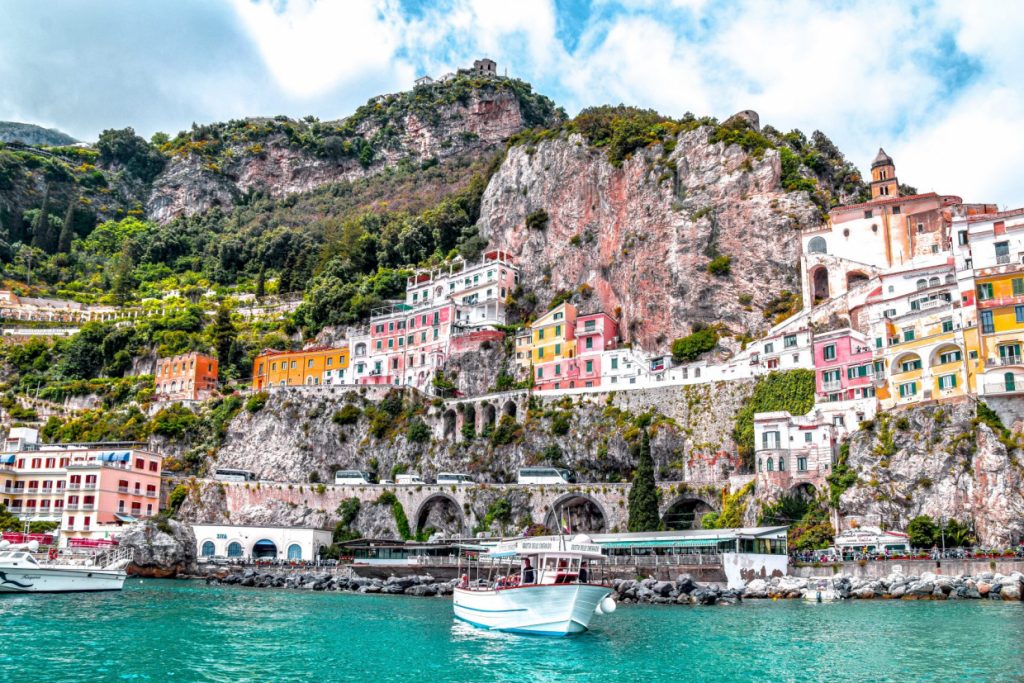 The Amalfi coast shoreline featuring pastel buildings and a white boat on the italian waters