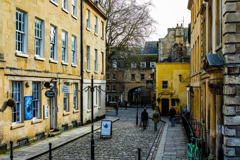 the cobble stone streets of Bath in England framed by yellow buildings and dotted with tourists