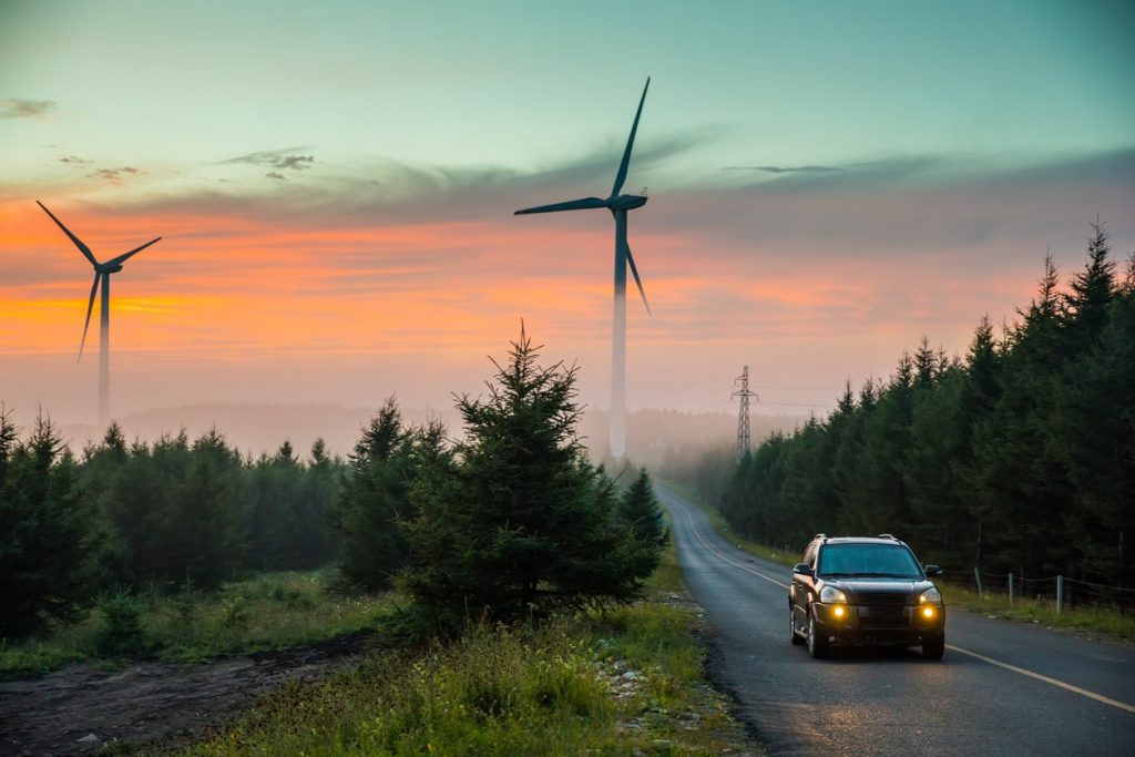 car drives at sunset past wind turbines