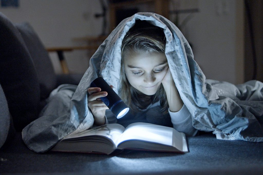 girl reading with a flashlight under a blanket