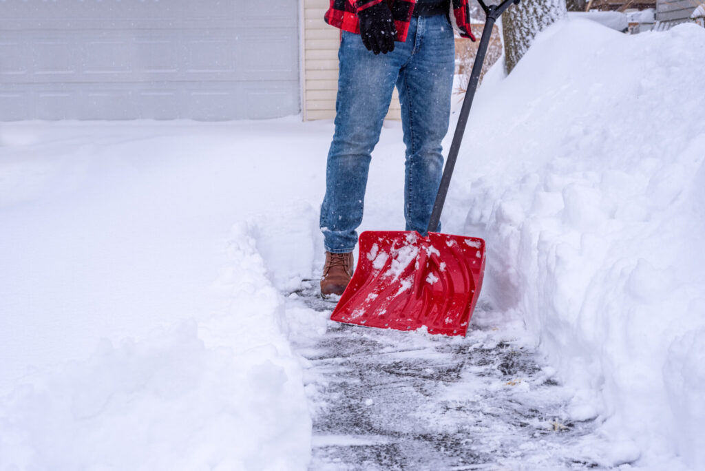 Man shoveling deep snow by hand with a red snow shovel