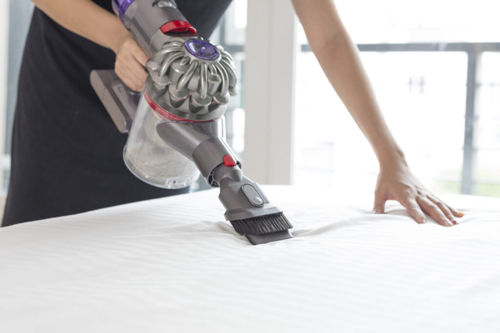 Woman disinfecting mattress with vacuum cleaner