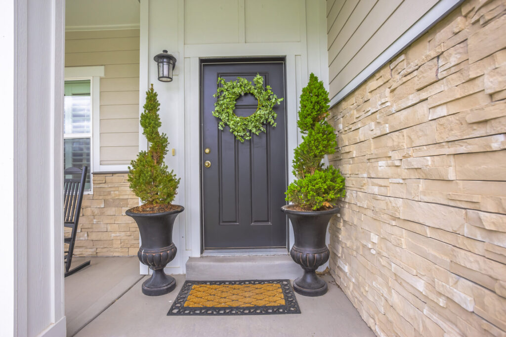gray front door of a home with green wreath and flanked by tall potted plants