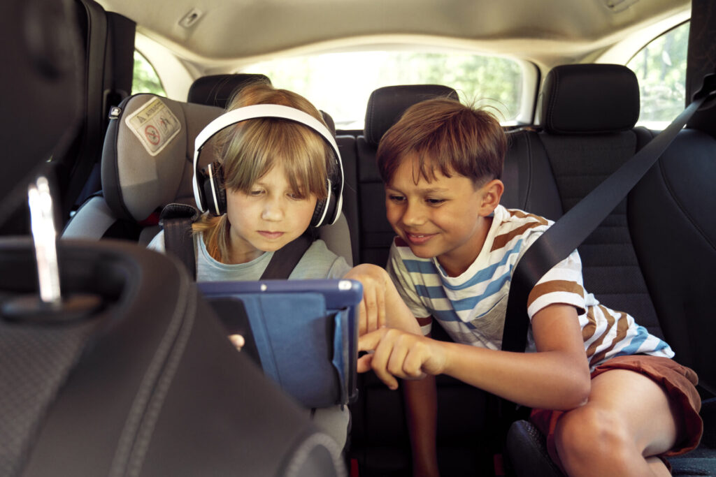 Happy siblings on rear seat of car with tablet