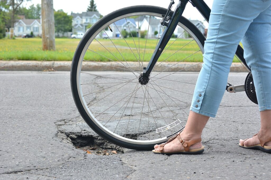 A cyclist walks their bike over a pothole