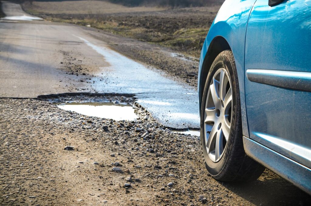 A blue car appraoches a pothole on a rough road