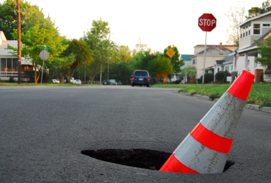 A traffic cone is placed in a deep pothole on a residential street