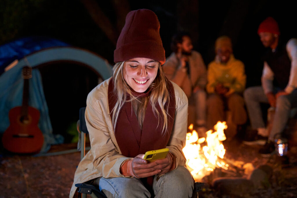 woman sitting outside in a camping using phone to be connected and sending messages happy.