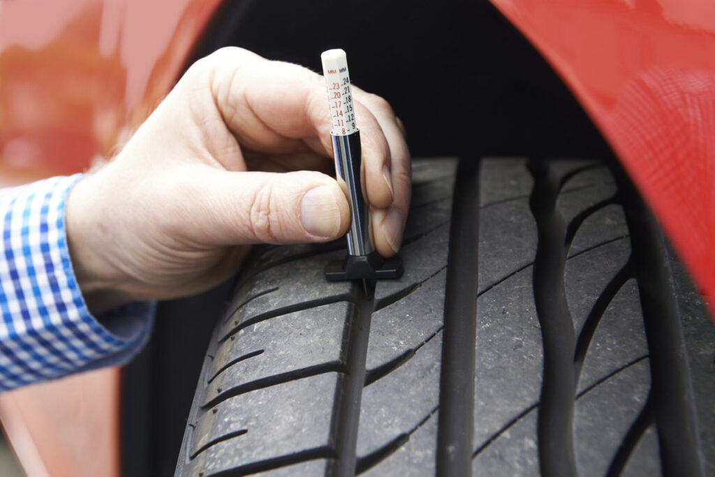 Close-Up Of Man Checking Tread On Car Tyre With Gauge