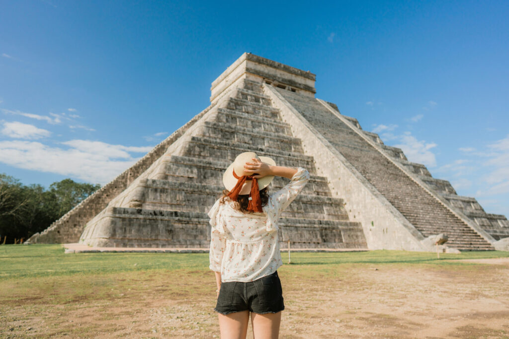 Rear view of young Caucasian woman in hat standing on the background of Chichen Itza pyramid in Mexico