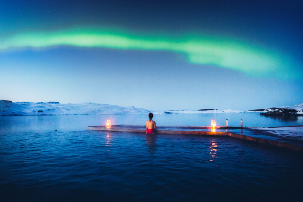 woman enjoying the scenic view of the Northern Lights above the lake and pool in Iceland