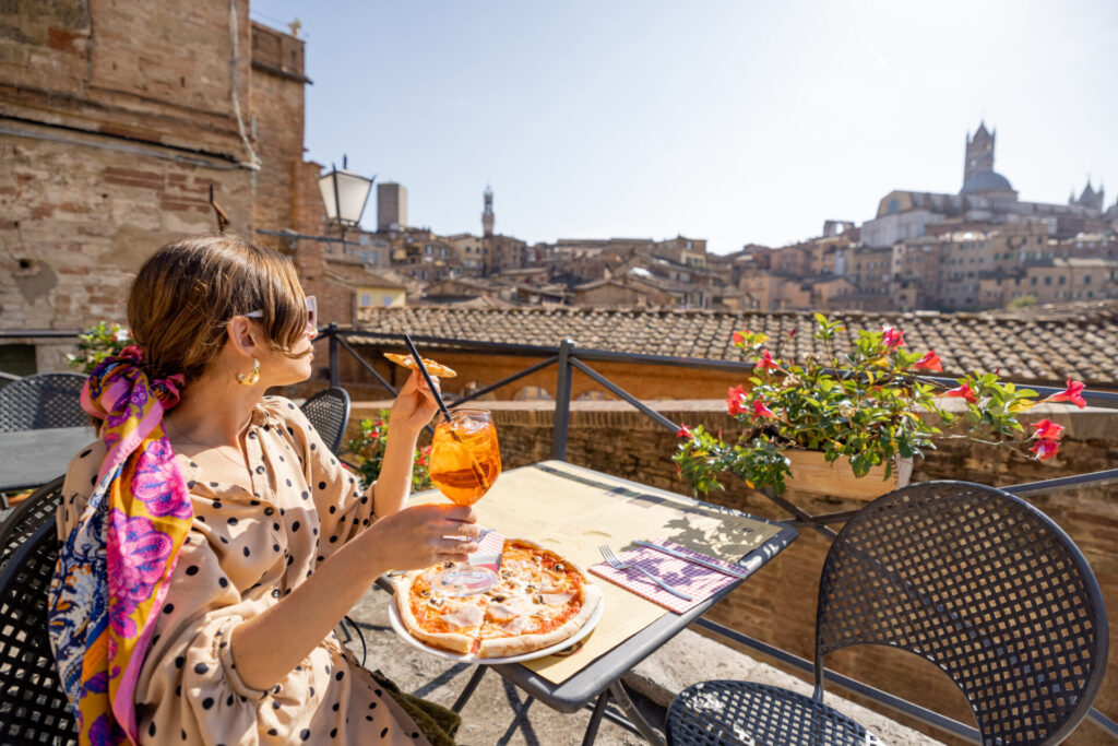 woman having lunch with pizza and wine at outdoor restaurant in Siena town