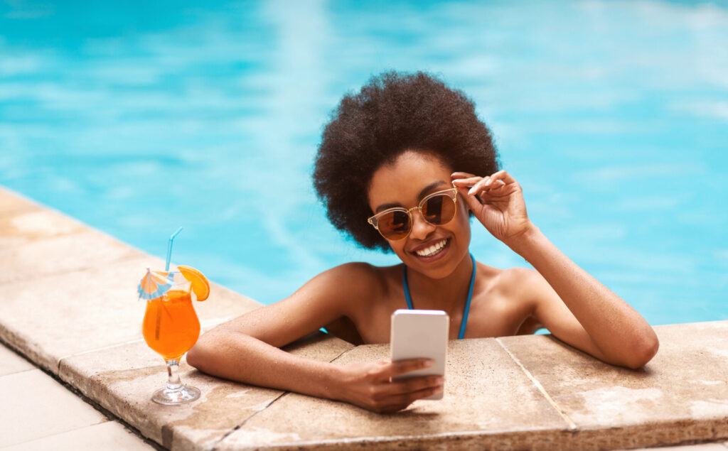 woman with tropical cocktail browsing internet on smartphone at swimming pool
