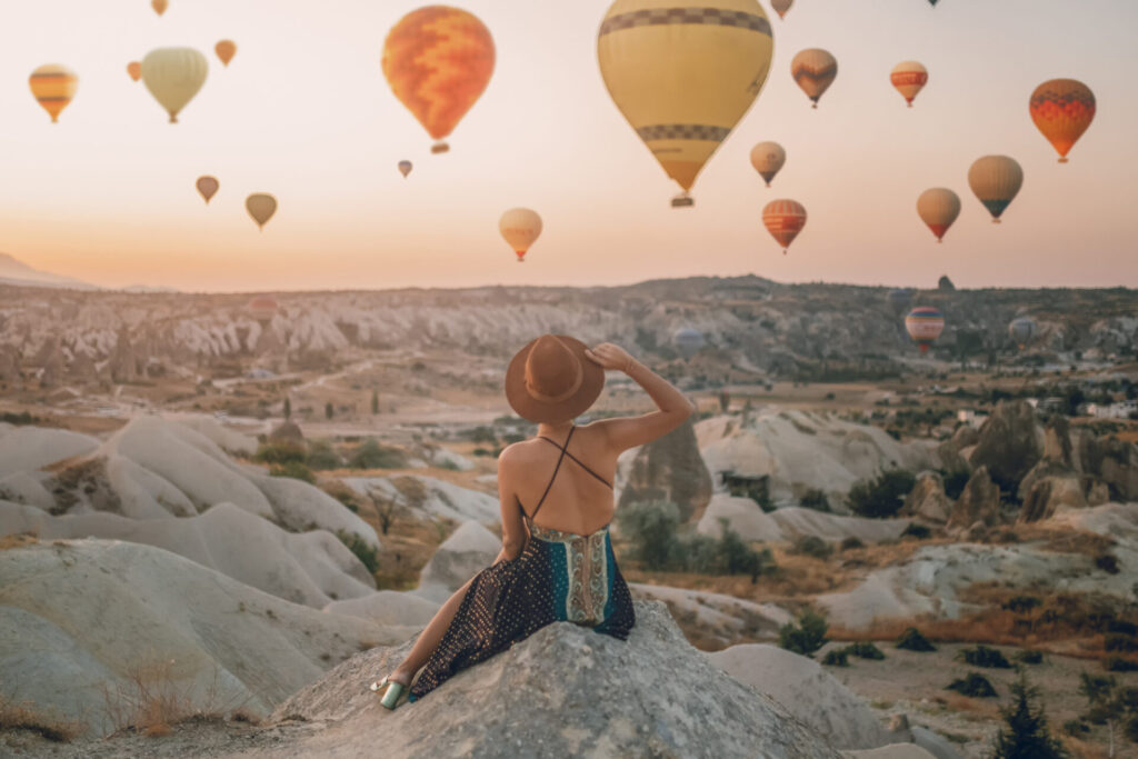 Woman Sitting On The Ground Watching Balloons Looking At The Valley. Cappadocia sunrise