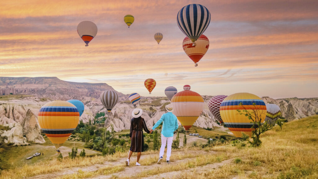 Cappadocia Turkey during sunrise, couple mid age men and woman on vacation in the hills of Goreme Capadocia Turkey, men and woman looking sunrsise with hot air balloons in Cappadocia