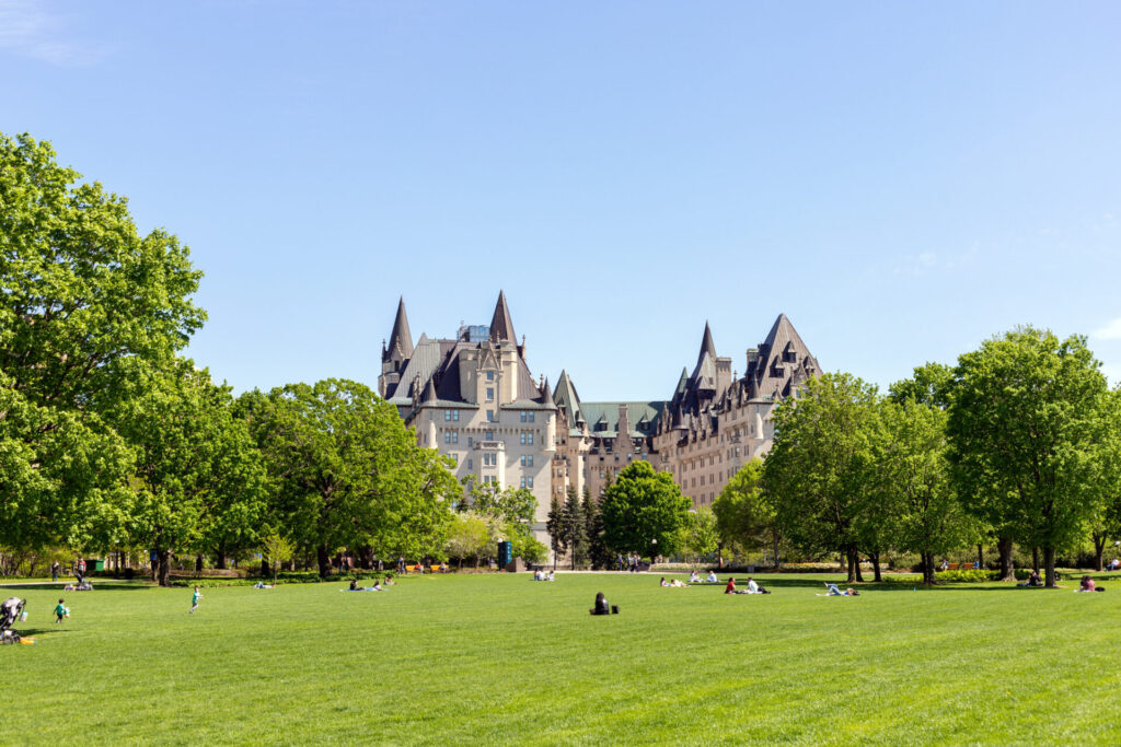 People in Majors Hill Park in spring. Fairmont Chateau Laurier Hotel building in city park in downtown Ottawa, Canada